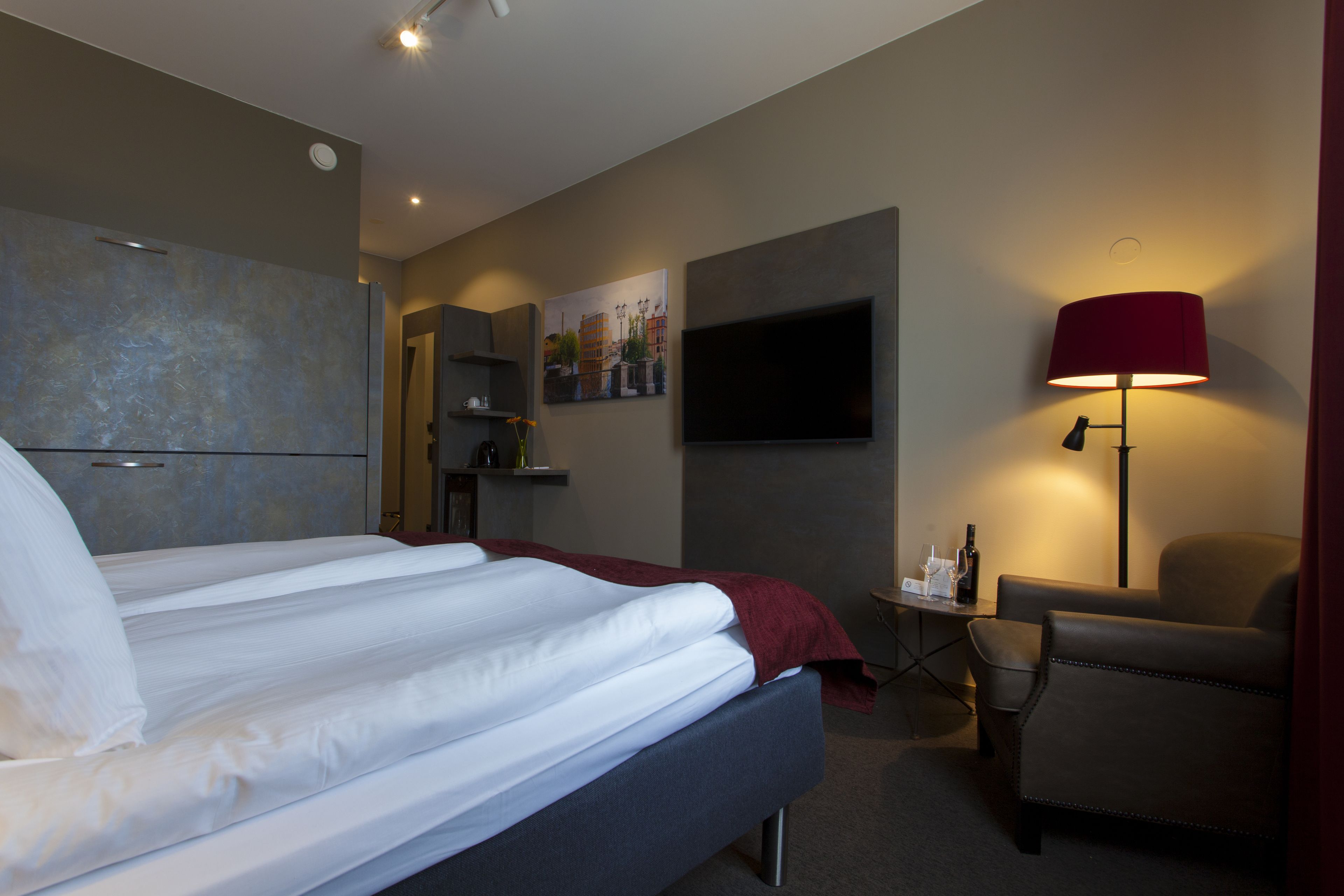 A hotel room with a bed, a desk, a chair, a TV, and a painting on the wall.