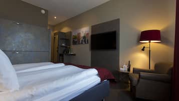 A hotel room with a bed, a desk, a chair, a TV, and a painting on the wall.
