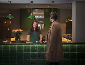 A bar area with a green tiled backsplash, two pendant lights, and a vase with flowers.