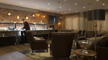 Una hall d'albergo moderna con una parete in mattoni, un'area bar, sedute in pelle e un'ampia lampada da terra.
