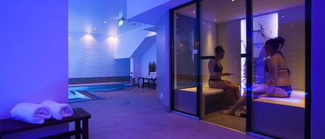 A spa area with a massage room, a bench with towels, and a pool in the background.