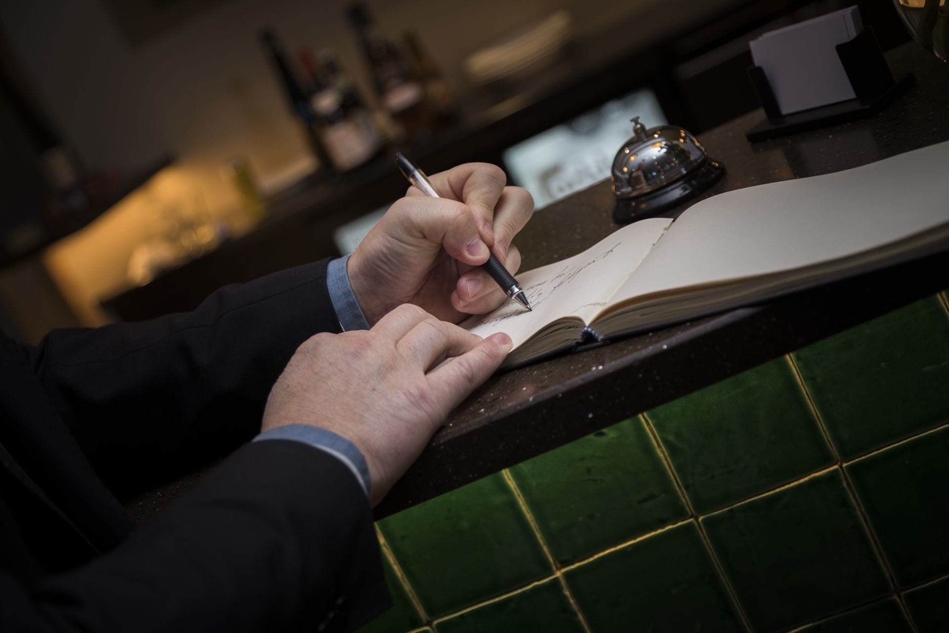 A person writing in a notebook at a counter with a green tiled backsplash.
