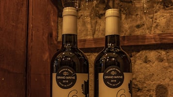 Två flaskor Grand Mayne-vin står på en trähylla, och i bakgrunden hänger vinglas.