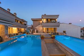 A modern poolside area with a large rectangular pool, a staircase leading to a second floor, and outdoor seating. - Kassandra Village Resort (Kassandra)