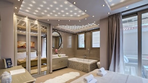 A modern hotel room with a large bed, a walk-in closet, a bathroom with a bathtub, and a large window. - Kassandra Village Resort (Kassandra)