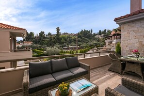 A balcony with a wicker sofa, a dining table set, and a magazine. - Kassandra Village Resort (Kassandra)