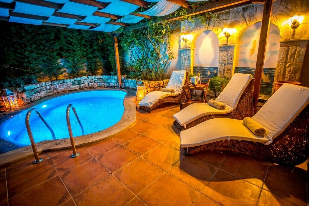 A poolside area with lounge chairs, a stone wall, and a pergola.