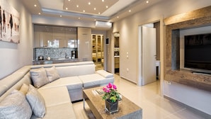 A modern living room with a sectional sofa, a coffee table with a plant, and a large flat-screen TV mounted on the wall. - Kassandra Village Resort (Kassandra)