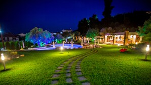 A well-lit garden pathway leading to a building with a fountain, surrounded by greenery and illuminated by various lights. - Kassandra Village Resort (Kassandra)