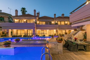 A luxurious pool area with a clear blue pool, outdoor seating, and a well-lit building with multiple balconies. - Kassandra Village Resort (Kassandra)