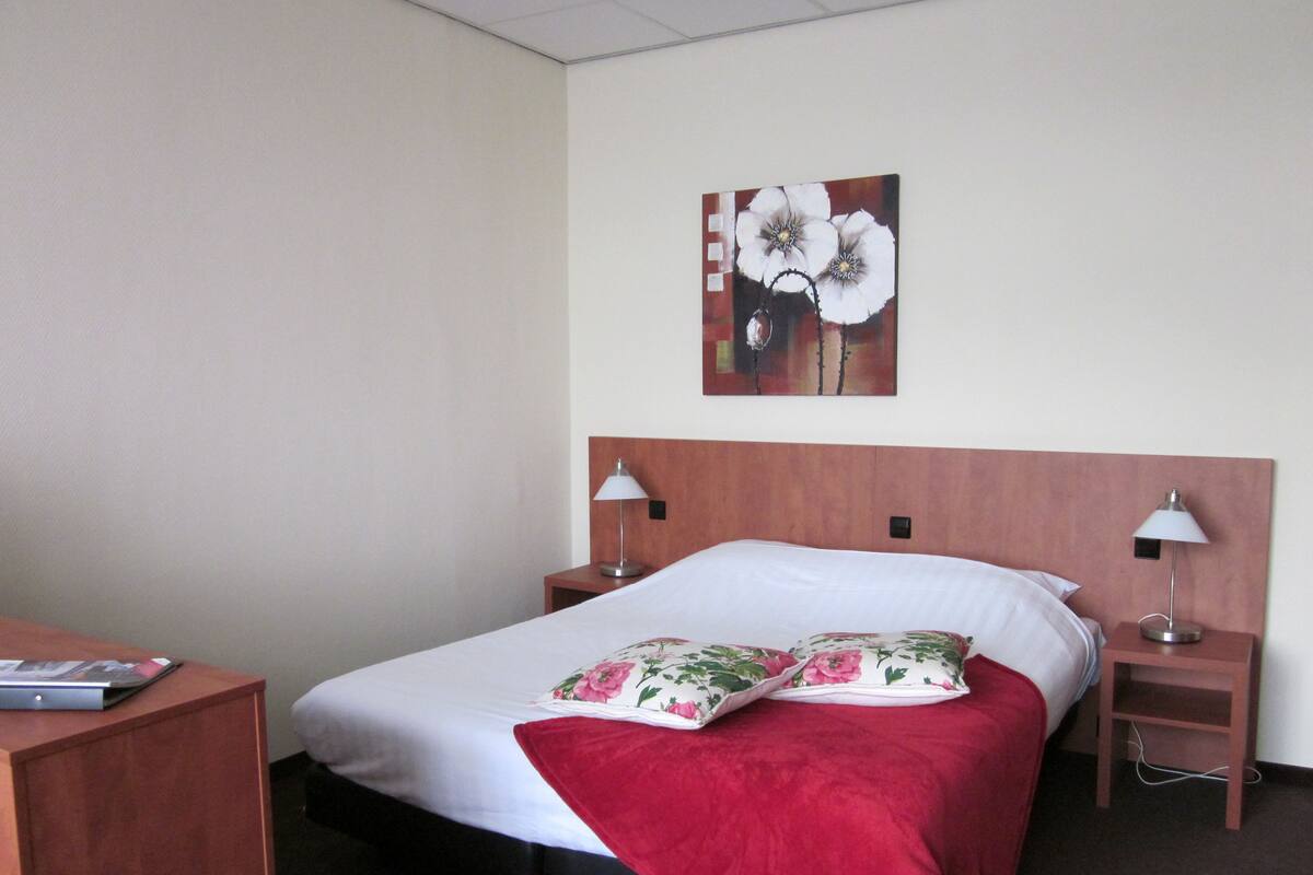 A hotel room with a bed, two bedside tables, a desk, and a wall-mounted painting.