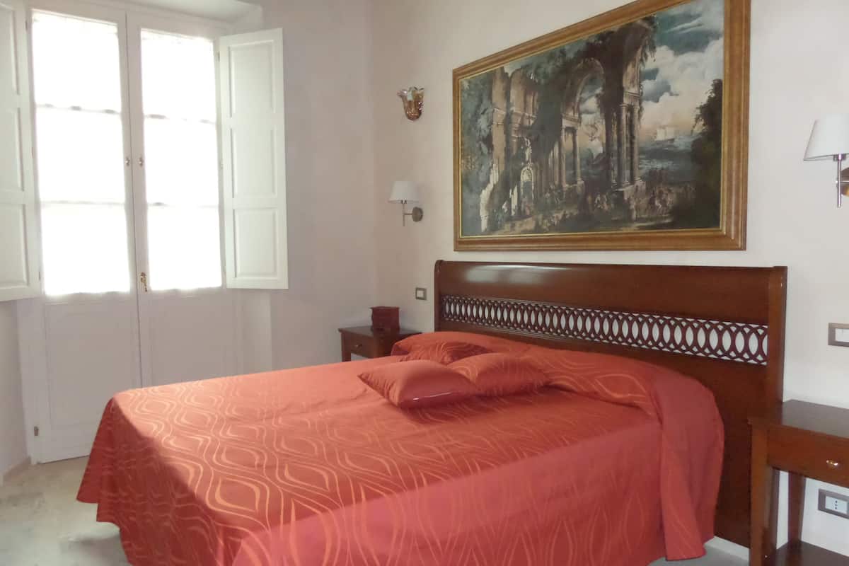 A bedroom with a bed, a painting, and a window.
