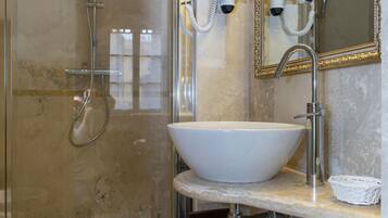Un bany amb plat de dutxa tancat amb vidre, un lavabo blanc i un mirall amb una estructura ornamentada.