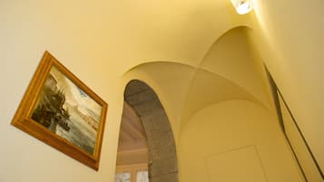 An interior corridor with a framed painting on the wall, an arched stone structure, and a light fixture.