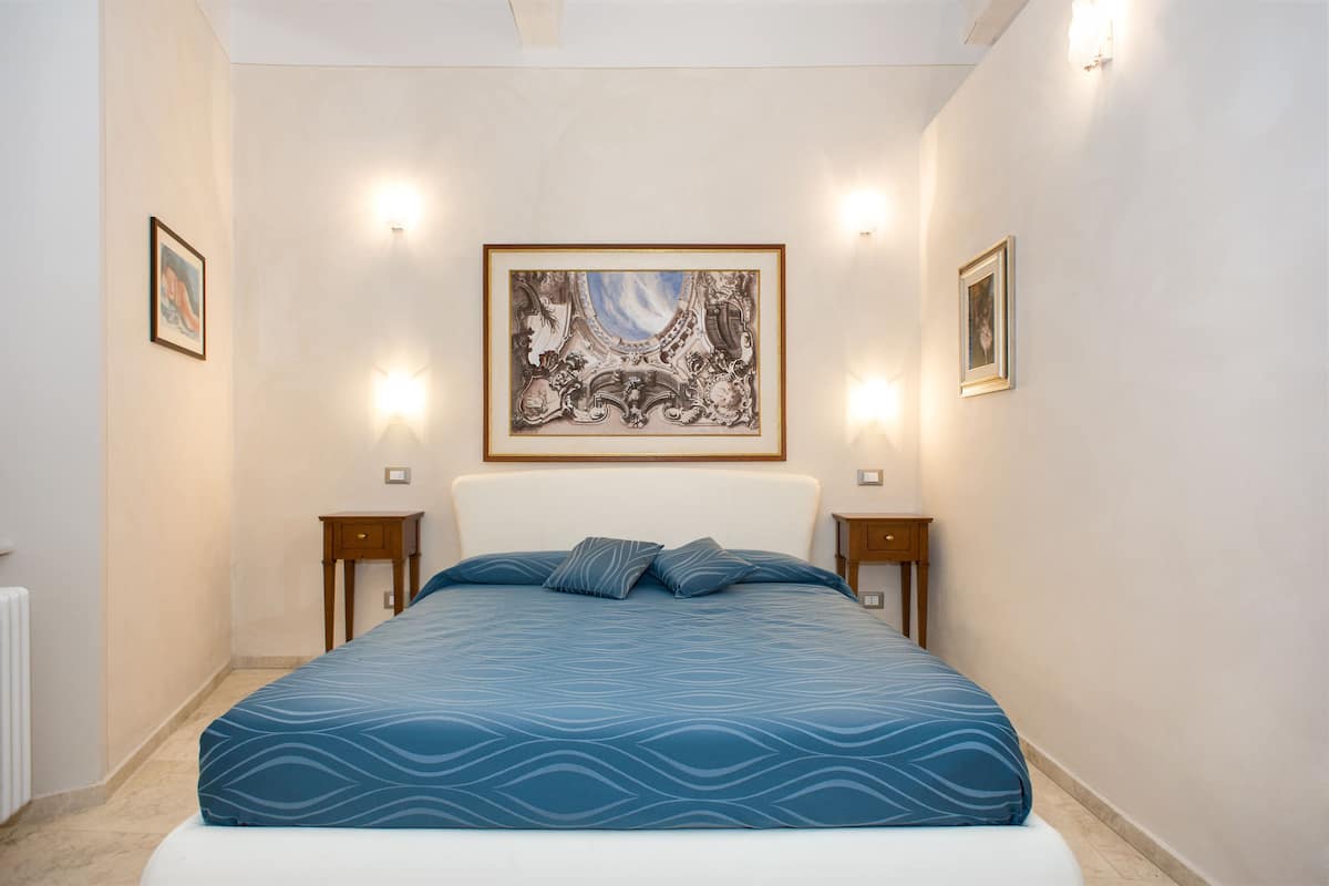 A bedroom with a large bed, two bedside tables, and a framed artwork on the wall.