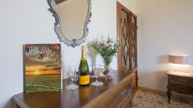 Un aparador de madera con un espejo, una botella de champán y un libro titulado "Toscana & Chianti".