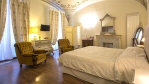 Un dormitorio con una cama grande, dos sillones, un aparador, un televisor y una chimenea.