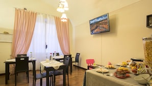 Un comedor con mesas y sillas de madera, un televisor en la pared y una mesa de buffet con diversos alimentos.
