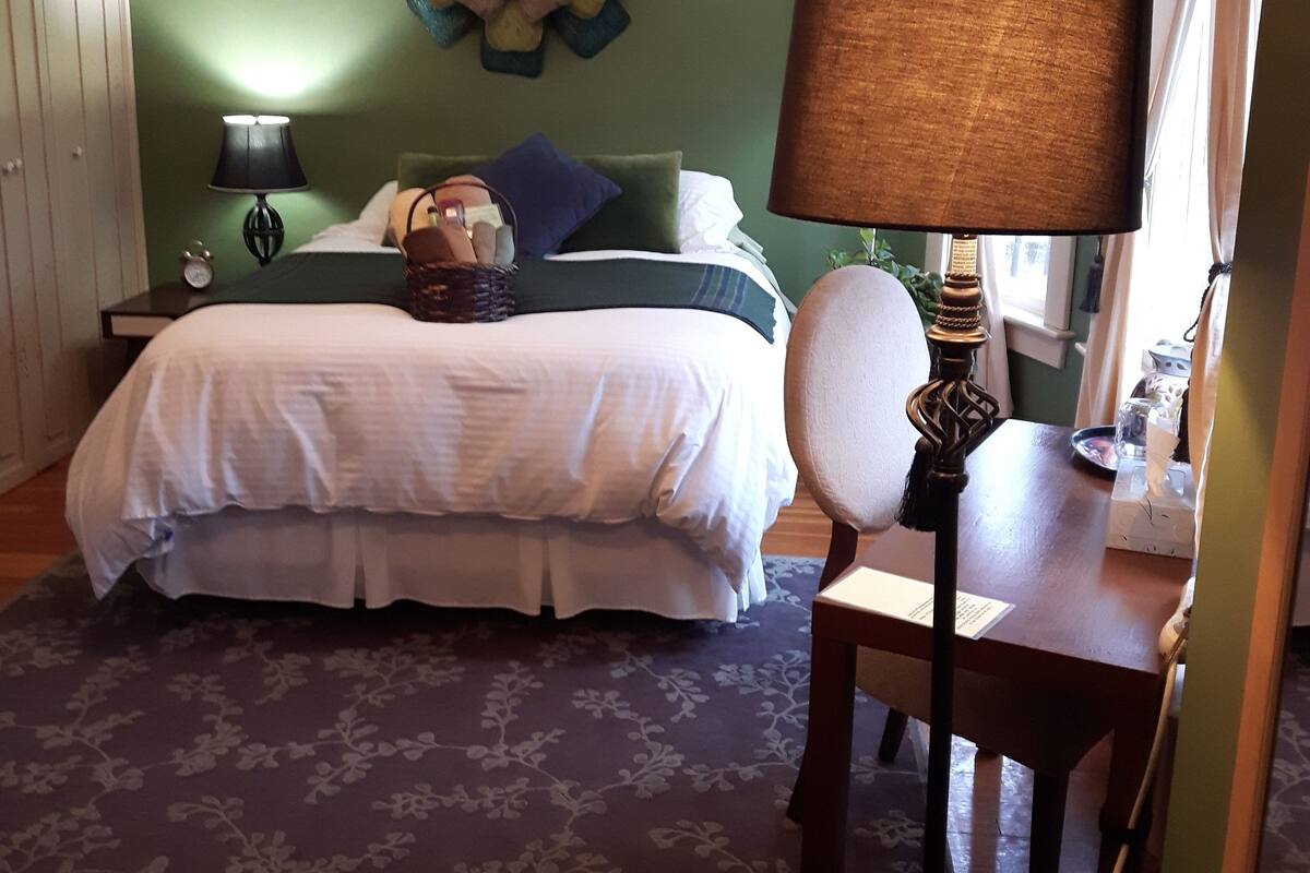 A bedroom with a bed, a nightstand, a lamp, a chair, and a decorative wall piece.