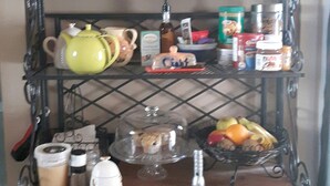 A metal shelf unit with various kitchen items, including jars, a teapot, and a fruit basket. - River Wynde Executive B&B (Calgary)