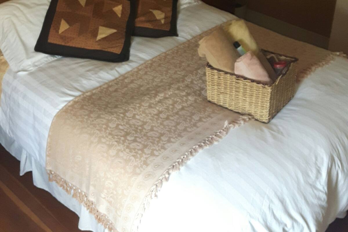 A neatly made bed with a patterned throw, a decorative pillow, and a small basket on the side.