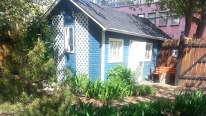 A blue house with a white fence, surrounded by a garden with various plants and a wooden deck. - River Wynde Executive B&B (Calgary)