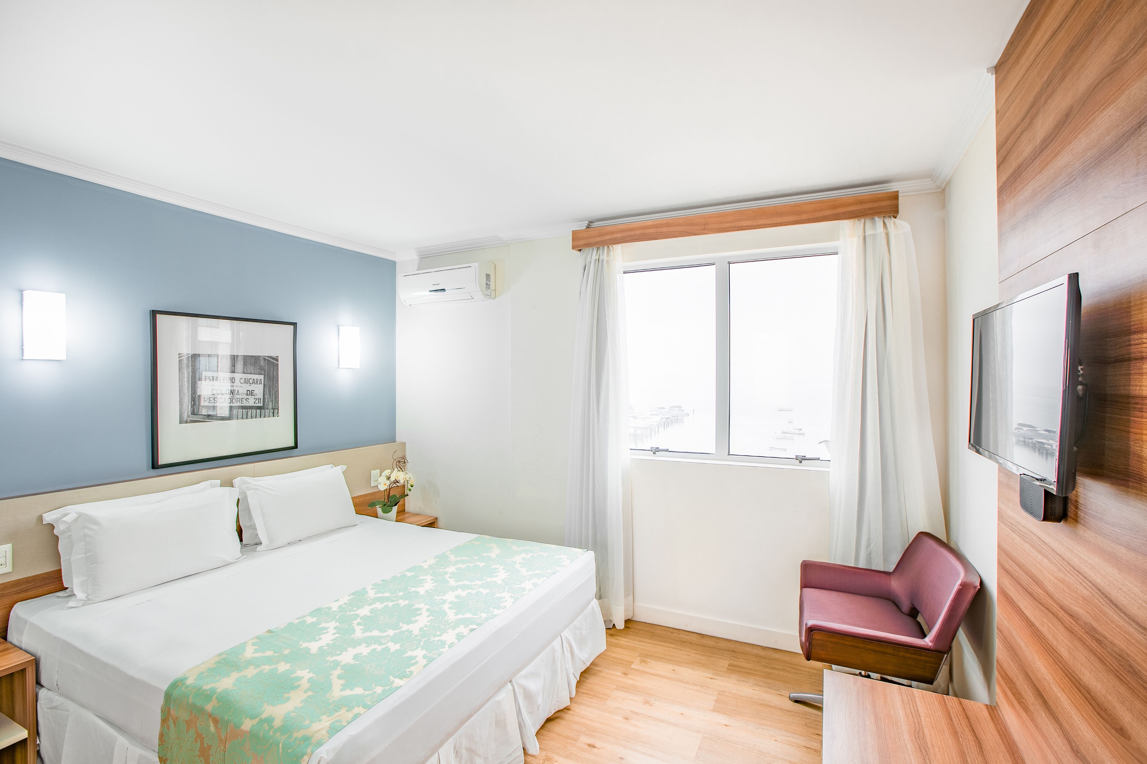 Una camera d'albergo con un letto, una sedia, una televisione e una finestra con tende.