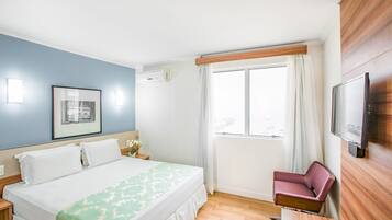 Una camera d'albergo con un letto, una sedia, una televisione e una finestra con tende.
