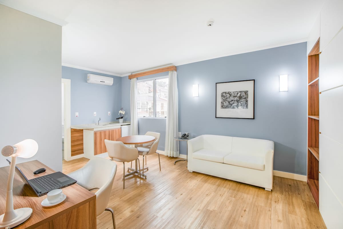 Ein modernes Wohnzimmer mit einem weißen Sofa, einem Holzespeisetisch mit Stühlen, einem Laptop und einer Schreibtischlampe.