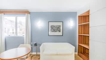 A room with a white sofa, a round table, a framed picture on the wall, and a wooden bookshelf.