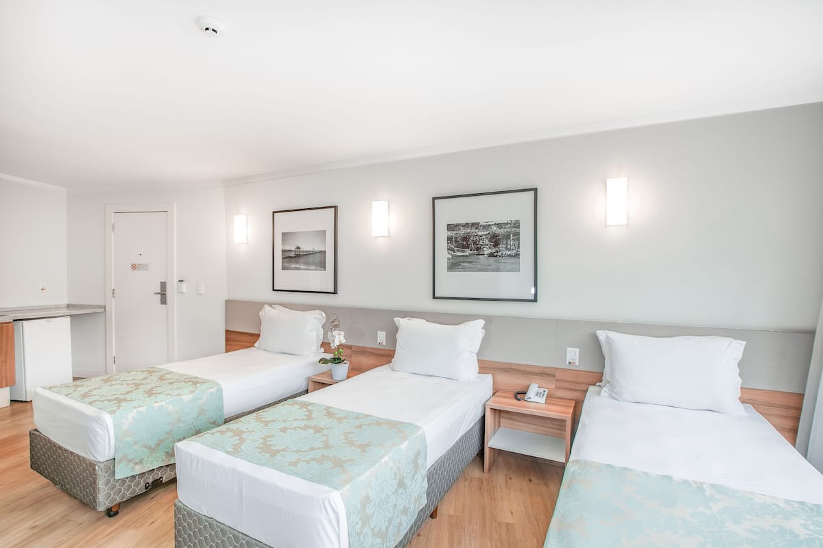 Ein Hotelzimmer mit drei Betten, einer kleinen Küchenzeile und gerahmten Bildern an der Wand.