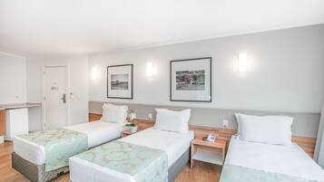 Habitación de hotel con tres camas, una kitchenette pequeña y fotografías enmarcadas en la pared.