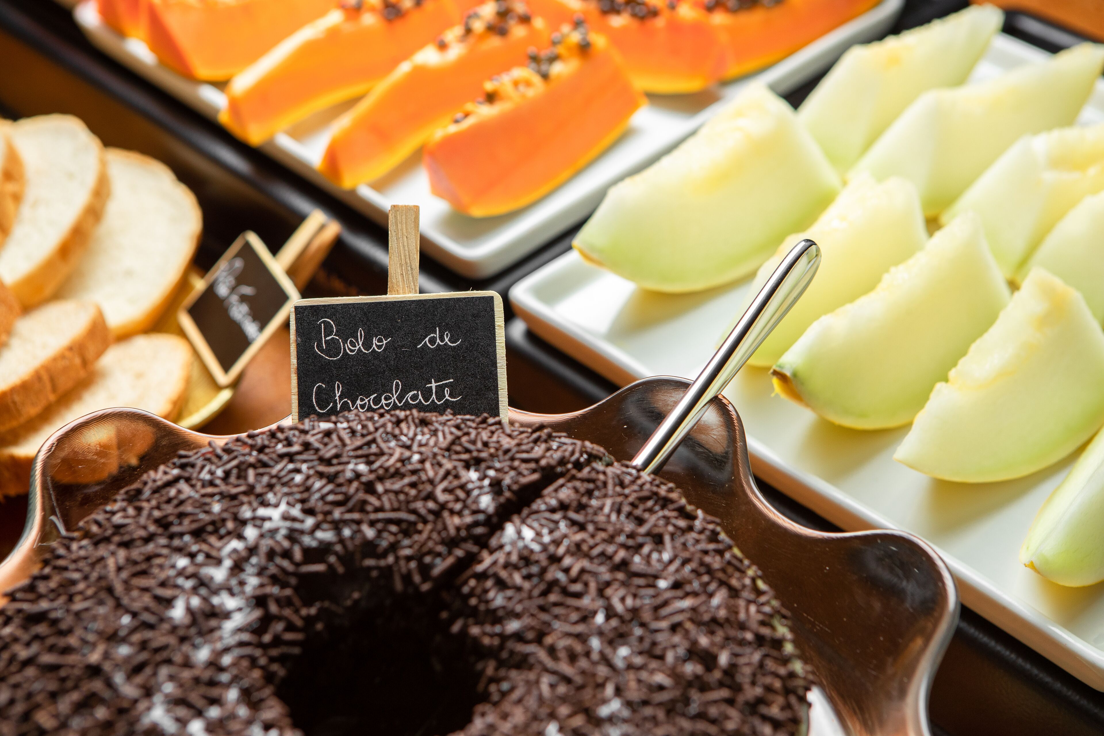 Un bufé de postres con pastel de chocolate, manzanas en rodajas y papaya.