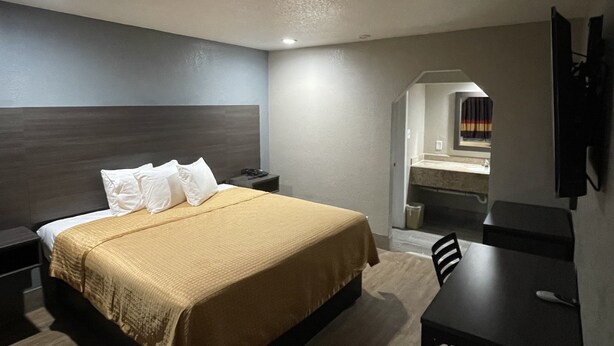 A hotel room with a bed, bedside table, desk, and a mirror. - Southmore Boulevard Motel (Houston)