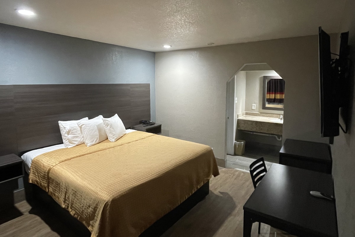 Quarto de hotel com cama, mesa de cabeceira, escrivaninha e espelho.
