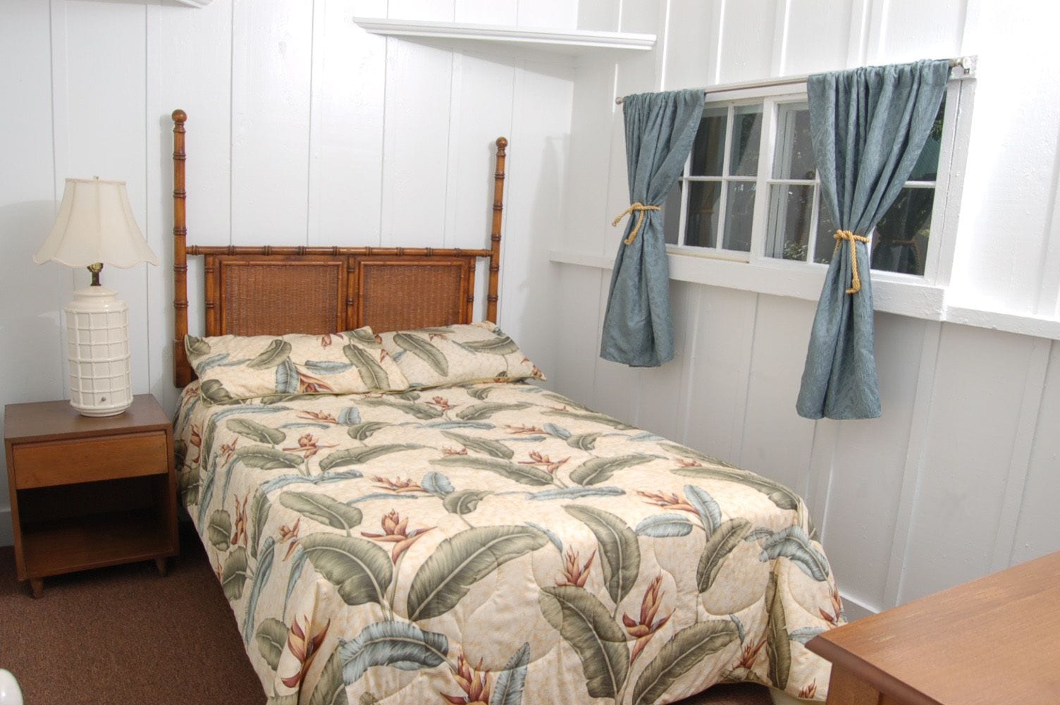 Un dormitorio con una cama de madera, una mesita de noche con lámpara y una ventana con cortinas.