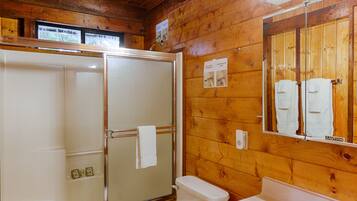 A wooden cabin bathroom with a shower, toilet, and sink.