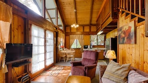 Interior acolhedor de uma cabana, com decoração em madeira, uma sala de jantar, um sofá e uma televisão.