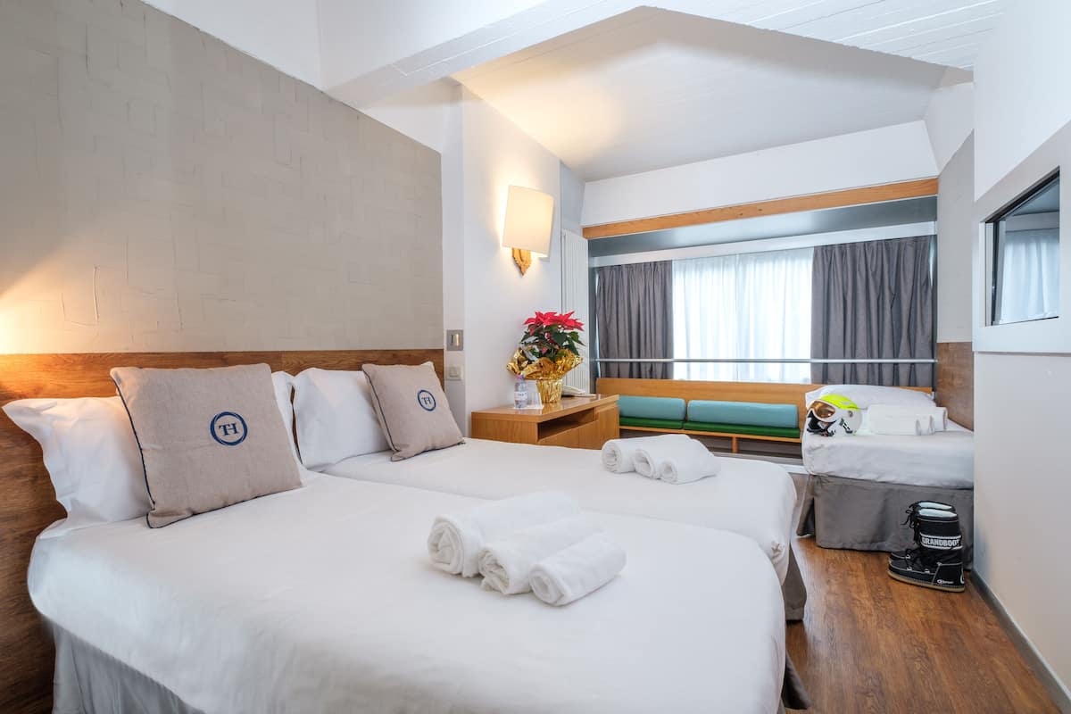 A hotel room with two beds, a wooden headboard, a nightstand with a lamp, a window with curtains, and a view of the outside.