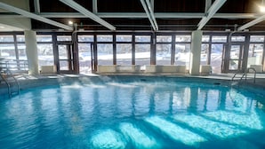 Ein Hallenbad mit klarem Wasser, Holzbalken und großen Fenstern, die einen Blick auf eine verschneite Landschaft bieten.
