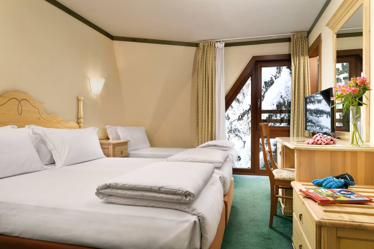 Camera d'albergo con un letto grande, una scrivania con sedia, una finestra con tende e vista su alberi.