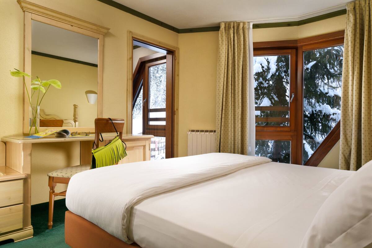 Una camera d'albergo con un letto, una scrivania, una sedia, uno specchio e una finestra con tende.