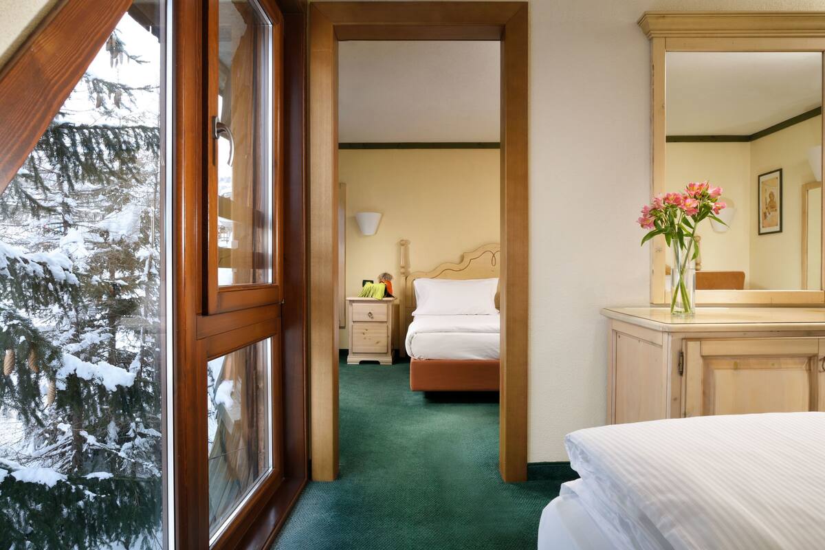 Una camera d'albergo con una porta in legno, un letto con biancheria bianca, un comodino con una lampada e un vaso con fiori.