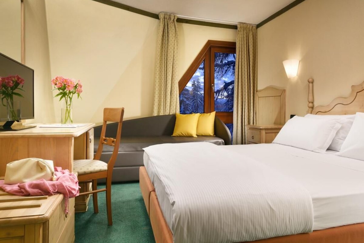 A bedroom with a bed, a desk, a chair, and a window with curtains.