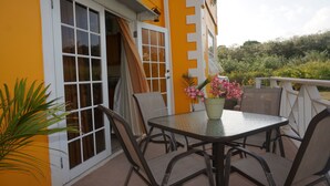 An outdoor patio with a table and chairs, a potted plant with flowers, and a view of greenery in the background. - Faith's Villa of Tobago (Scarborough)