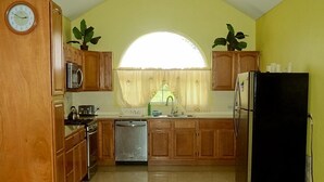 A kitchen with wooden cabinets, a microwave, a stove, a sink, and a refrigerator. - Faith's Villa of Tobago (Scarborough)