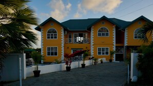 A yellow building with a balcony, potted plants, and a paved driveway. - Faith's Villa of Tobago (Scarborough)