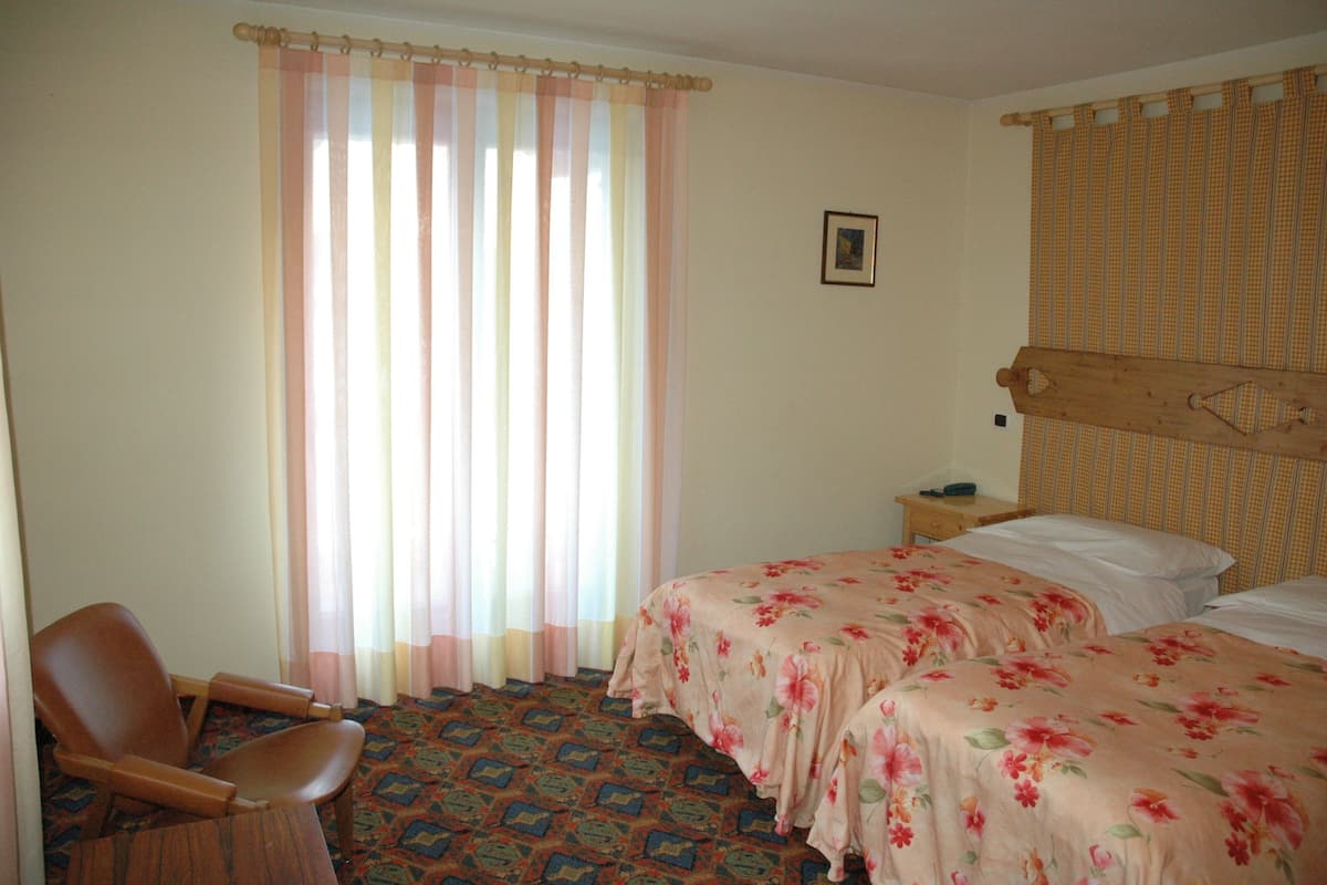 A hotel room with two beds, a chair, a nightstand, and a window with curtains.