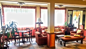 A spacious lobby with a checkered floor, a dining area with a table and chairs, and a seating area with sofas and a coffee table. - IHR Hotel Villa Emma (Canazei)