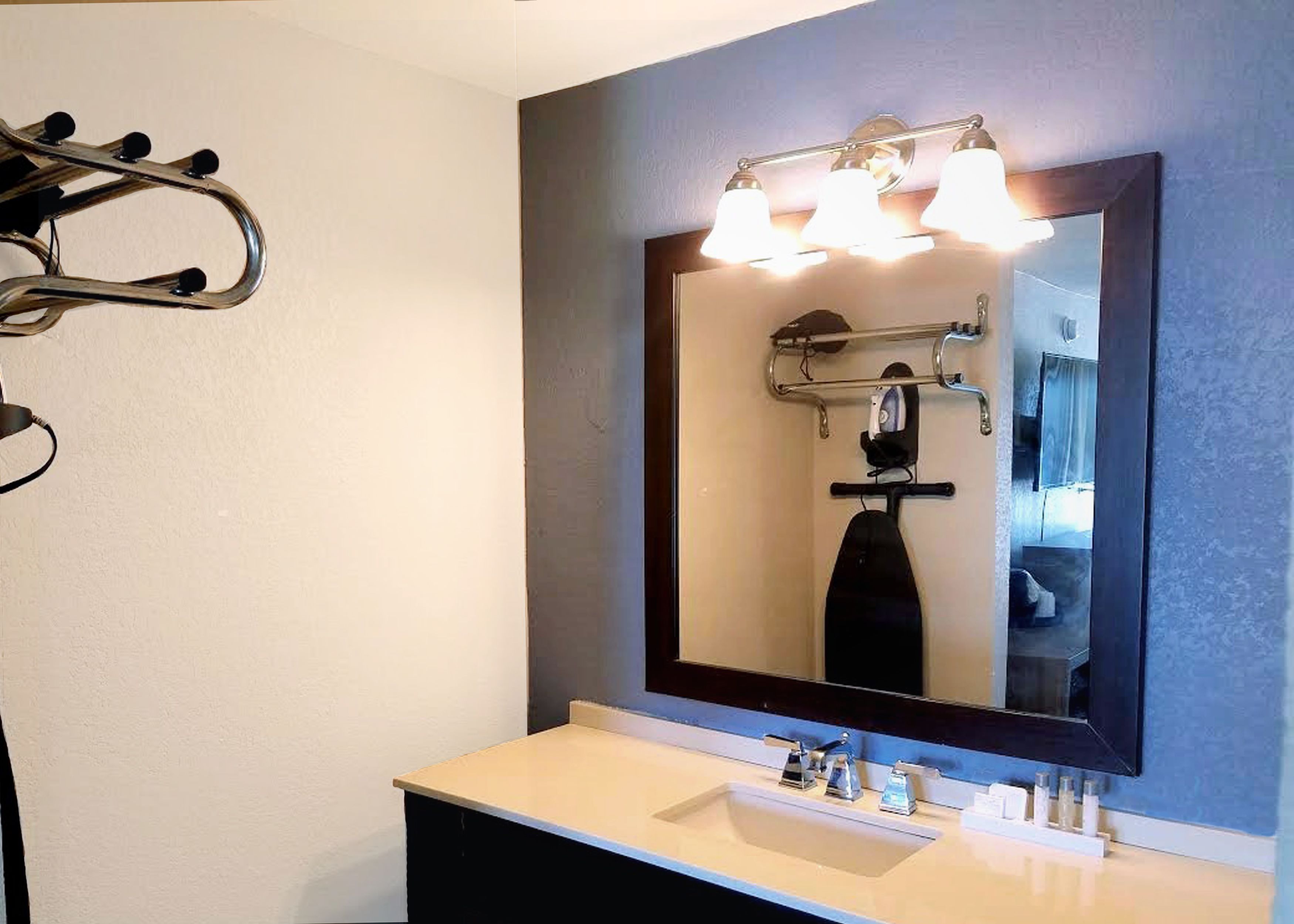 A bathroom with a large mirror, three light fixtures, a sink, and a towel rack.